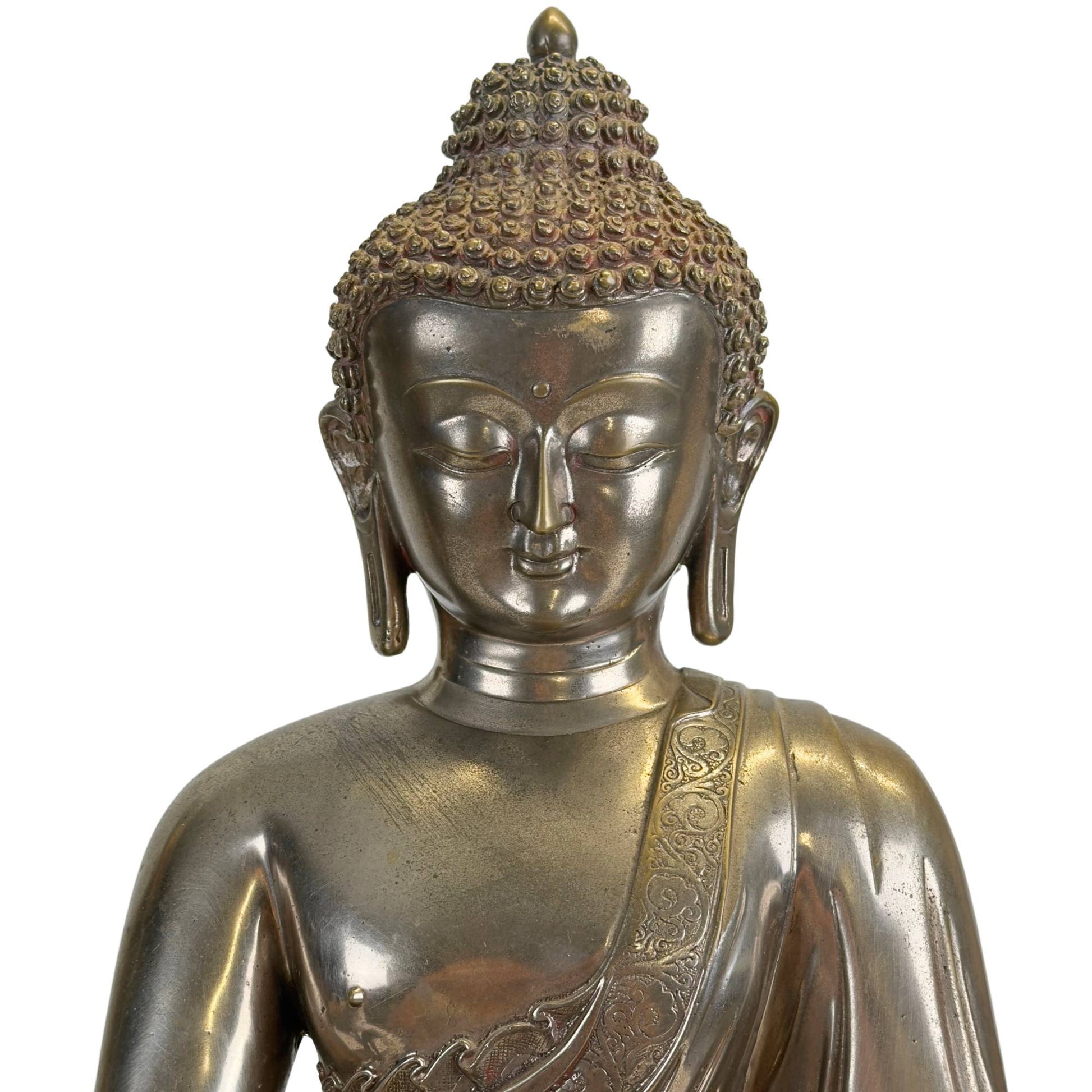 Detail van het gezicht van een antieke Newar Bhaisajyaguru in verzilverd brons met serene uitdrukking, amandelvormige ogen, fijn gemodelleerde lippen, urna en karakteristieke haarkrullen met natuurlijke slijtage en patina.