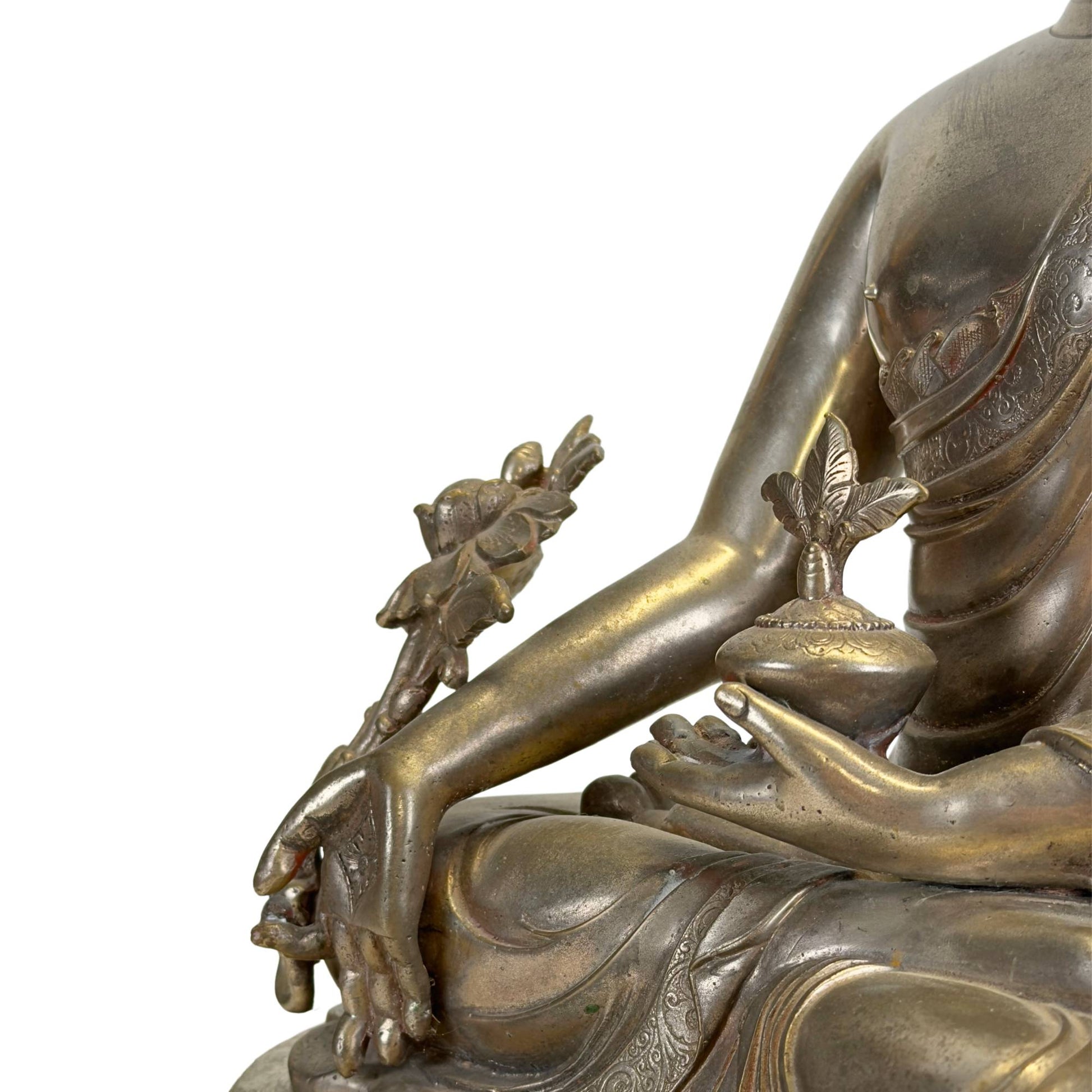 Detail van een antieke Newar Bhaisajyaguru in verzilverd brons met medicijnpot, myrobalanplant, fijn gegraveerde gewaden en natuurlijke slijtage die de hoge ouderdom onderstreept.